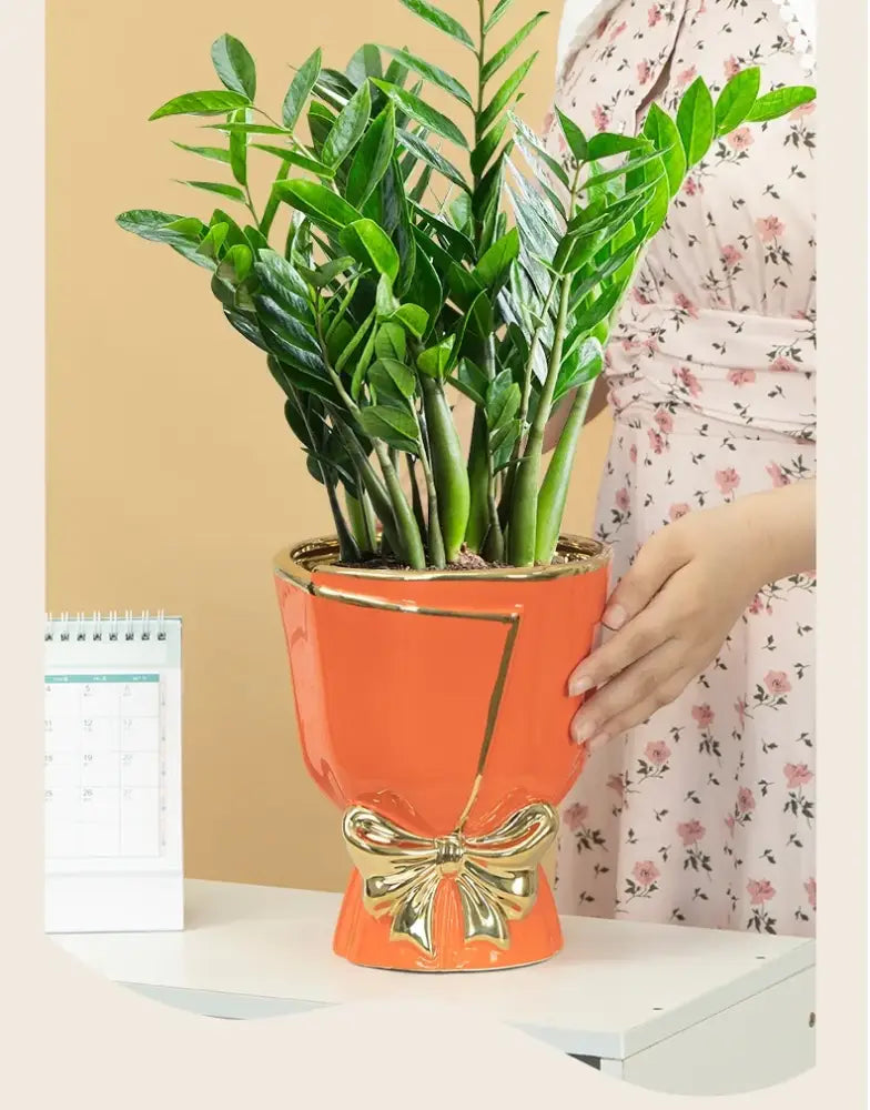 Orange ceramic vase with gold bow and geometric trim holding a lush green zz plant for modern nordic home decor