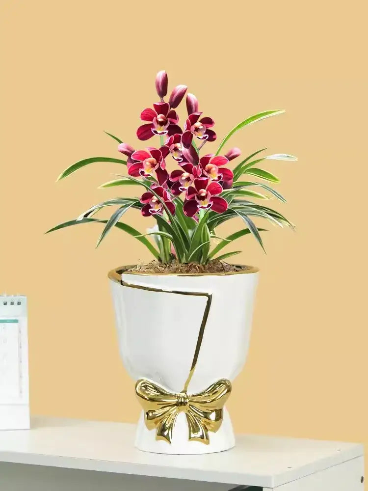 A white ceramic vase with gold geometric accents and bow detail holding deep red orchids for modern nordic home decor