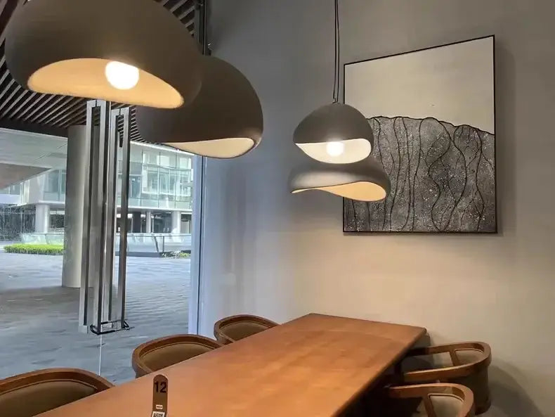 Modern gray pendant lights with soft dome-shaped shades hang above a wooden table in a modern nordic chandelier with warm light turn
