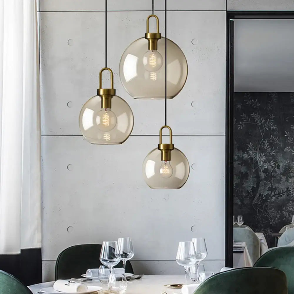Three brass fixture glass pendant lights hang above a dining table in the DecorBites™ modern Nordic pendant light design