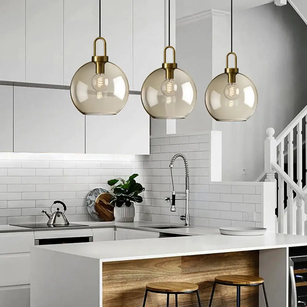 Three hanging decorbites™ modern nordic glass pendant lights with smoked glass globes and brass accents for kitchen use