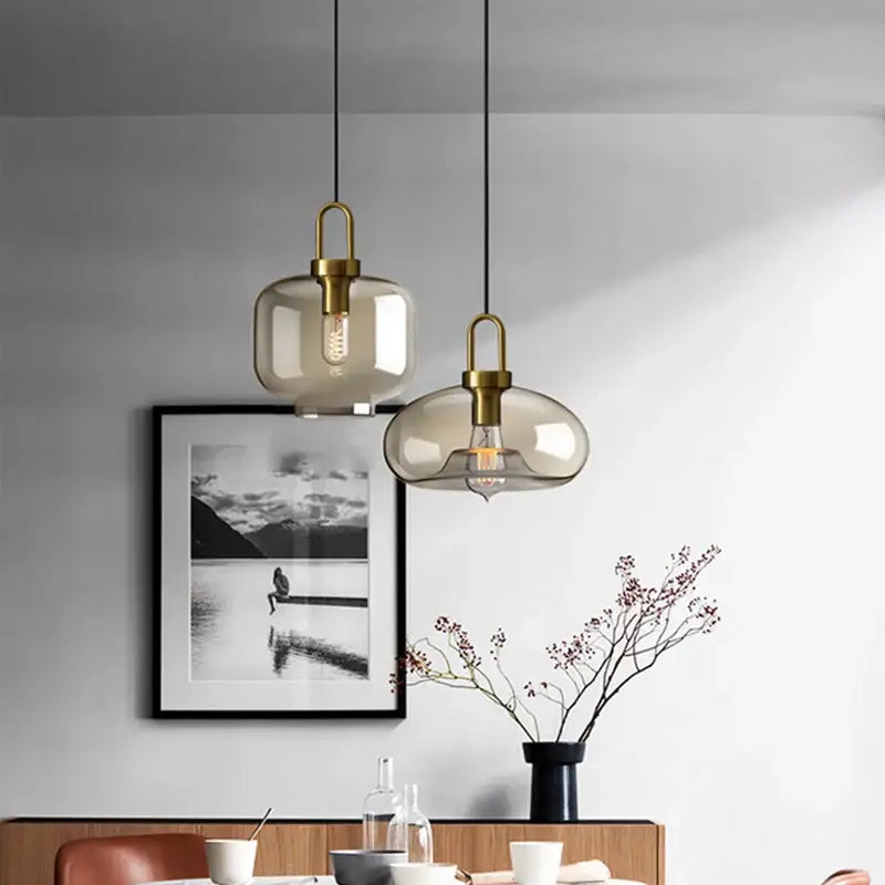 Two modern pendant lights with smoked glass shades and brass hardware for kitchen or restaurant by DecorBites™