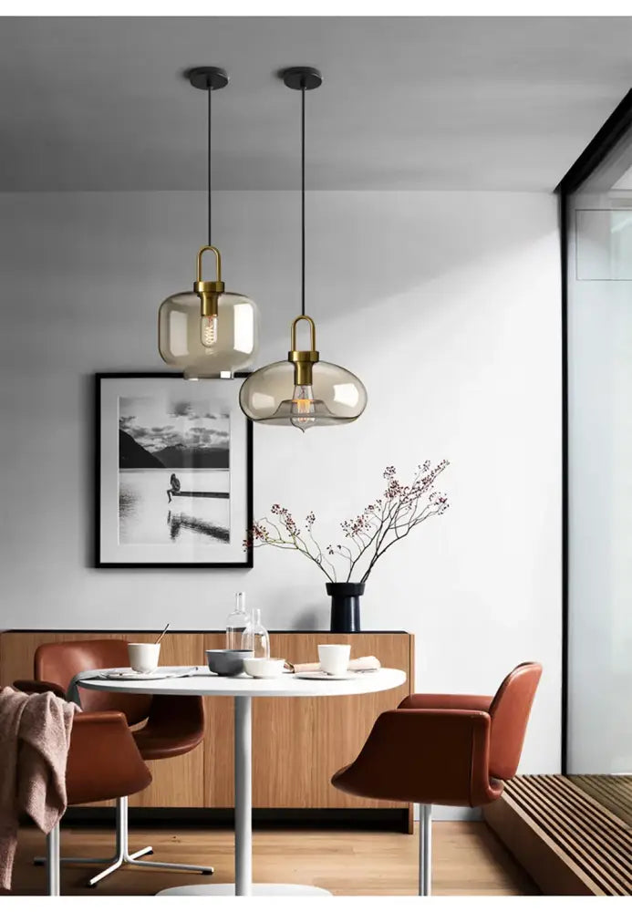 Two elegant DecorBites modern nordic glass pendant lights with smoked glass shades and brass accents hang above table