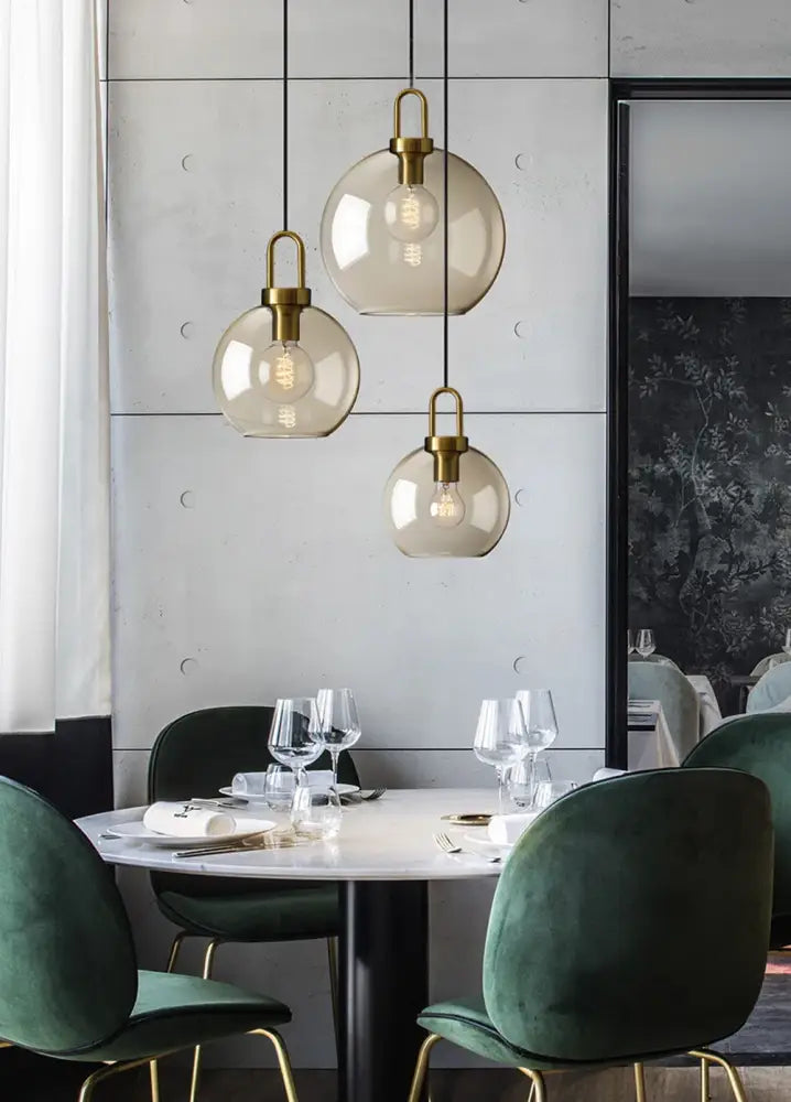 Three spherical glass pendant lights with brass fixtures hang above a dining table in a modern Nordic style pendant light setup