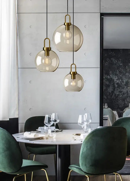 Three spherical glass pendant lights with brass fixtures hang above a dining table in a modern Nordic style pendant light setup
