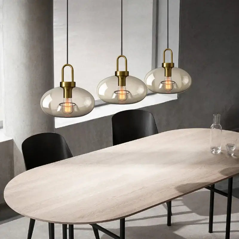 Three modern brass-finished decorbites glass pendant lights with smoke-gray shades for kitchen and restaurant use