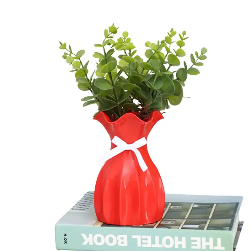 Red ceramic vase home with a fluted rim and white ribbon holding green artificial eucalyptus foliage for decor
