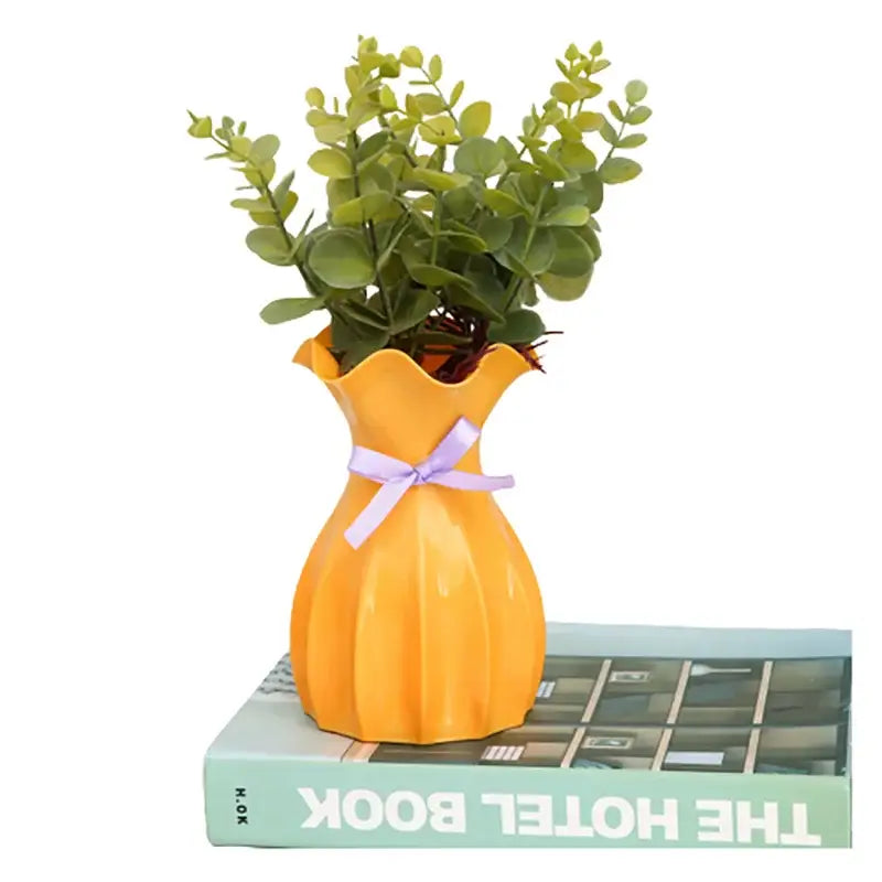 Vibrant orange ceramic flower vase home with fluted edges and lavender ribbon holding lush green artificial foliage