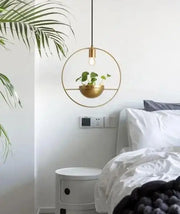 Gold-toned circular pendant light with a modern nordic planter featuring a hanging plant in a matching bowl