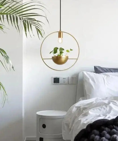 Gold-toned circular pendant light with a modern nordic planter featuring a hanging plant in a matching bowl