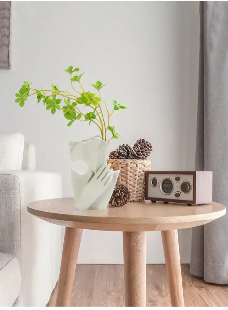 A white nordic style ceramic vase with an abstract sculpted design holding green foliage by decorbites™