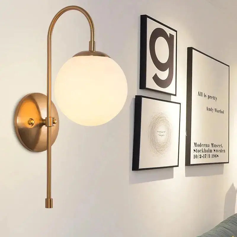 Brass-finished DecorBites modern Nordic wall lamp by Olsson with curved arm and frosted glass globe shade