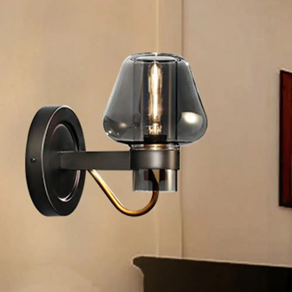 A sleek black wall-mounted lighting fixture with modern smoked glass mushroom shade and brass accent arm for bedroom use