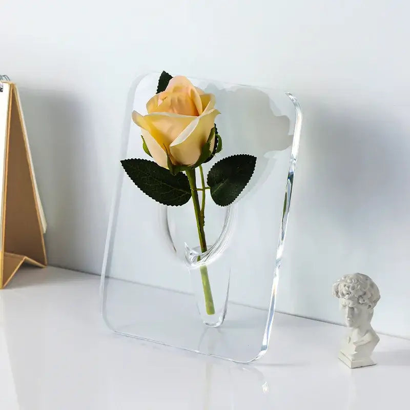 Decorbites™ modern transparent square acrylic vase holding a pale yellow rose with dark green leaves in a square vase