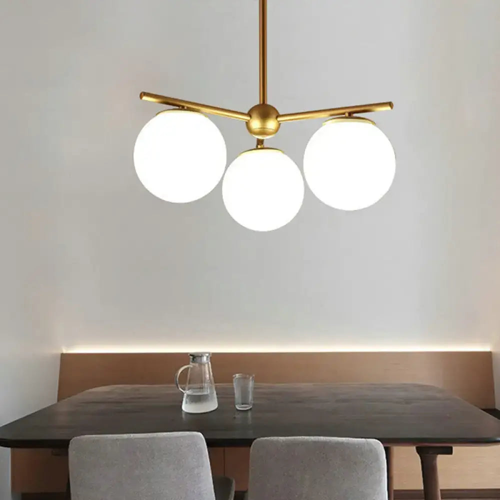 Gold-toned modern chandelier with three spherical white frosted glass shades for bedrooms by decorbites