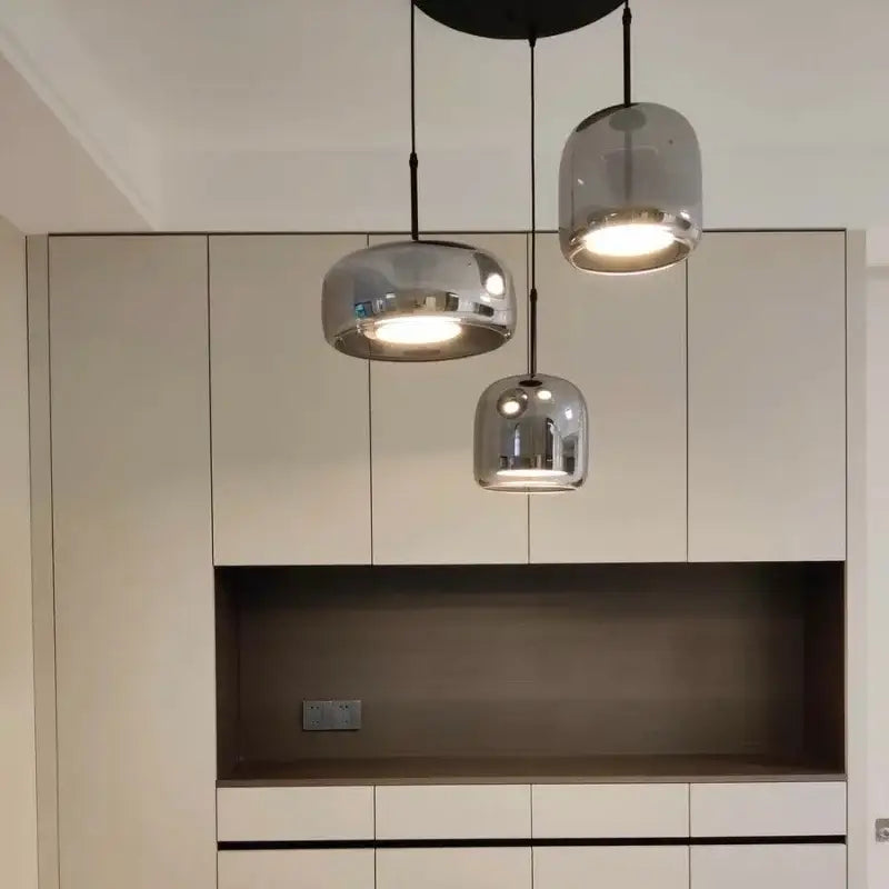 Three modern nordic pendant lights with chrome finish and amber glass domes hang above a built-in cabinet