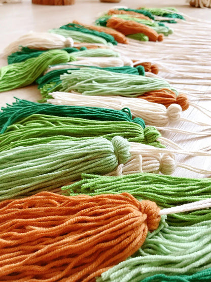 Rows of colorful yarn tassels in green orange and white on a light surface for moroccan bohemian wall decor tapestry