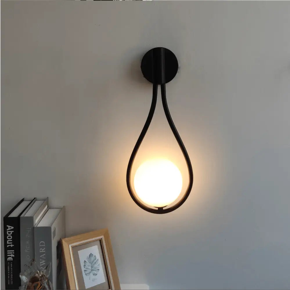 Black metal wall lamp with teardrop frame and warm glowing light in the DecorBites modern nordic wall lamp design
