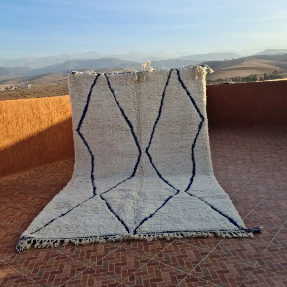 Cream-colored moroccan handmade amazigh rug with bold navy blue geometric patterns and fringed edges by DecorBites