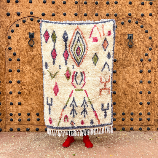 Cream-colored moroccan handmade azilal carpet with intricate red green navy geometric patterns and fringed edges by skilled artisans
