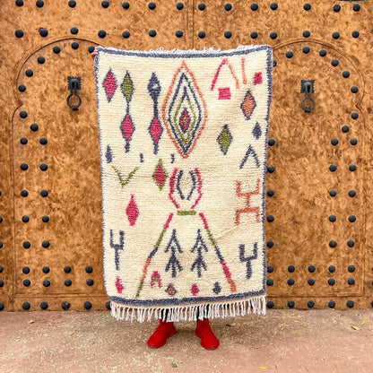 Cream-colored moroccan handmade azilal carpet with intricate red green navy geometric patterns and fringed edges by skilled artisans
