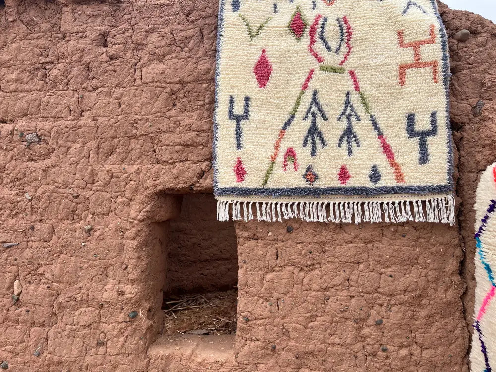 Cream-colored moroccan handmade azilal carpet by skilled artisans with geometric red blue and green patterns and fringed edge