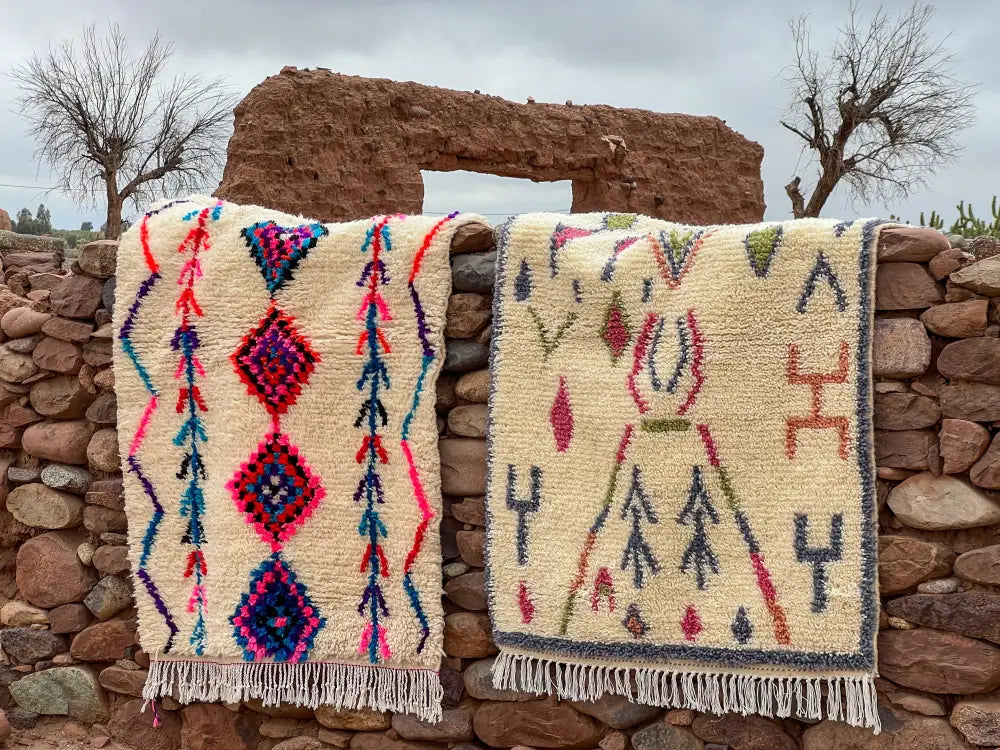 Two moroccan handmade azilal rugs with vibrant geometric patterns in pink blue purple and green on cream background by skilled artisans