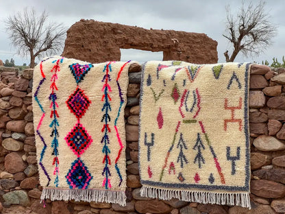 Two moroccan handmade azilal rugs with vibrant pink blue purple and green geometric patterns on cream background