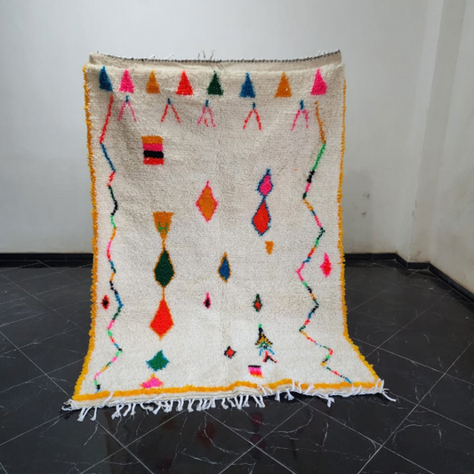 A vibrant cream-colored DecorBites™ moroccan handmade azilal rug with colorful geometric patterns and fringed edges