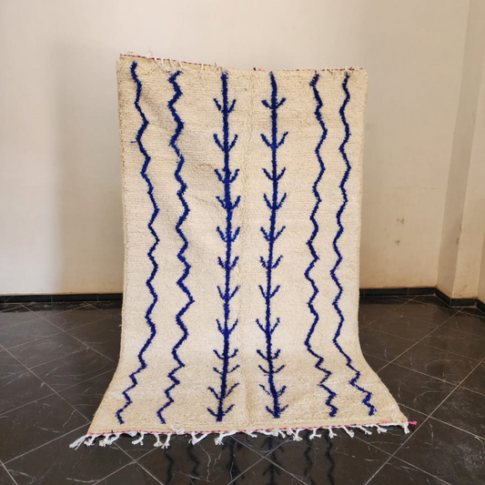 Cream-colored moroccan handmade azilal rug with bold blue zigzag and tree-like patterns and fringed edge 2.5m x 1.5m