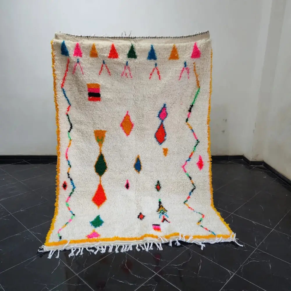 A vibrant cream-colored DecorBites™ moroccan handmade azilal rug with colorful geometric patterns and fringed edges