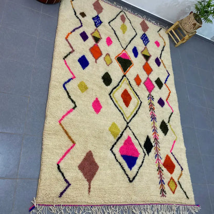 Cream-colored moroccan handmade azilal rug with vibrant pink blue orange and green geometric patterns on fluffy wool base