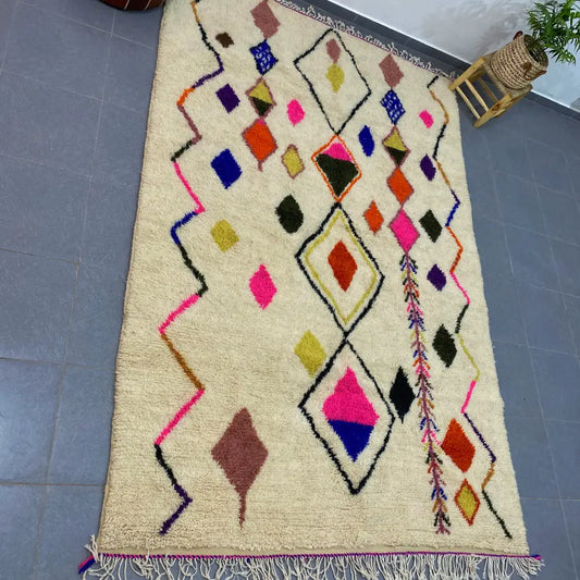 Cream-colored moroccan handmade azilal rug with vibrant pink blue orange and green geometric patterns on fluffy wool base