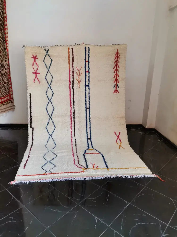 Cream-colored moroccan handmade azilal berber carpet with geometric red blue and black patterns supporting sustainable practices