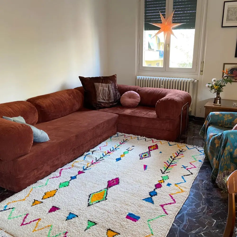 A plush rust-colored corduroy sectional sofa with rolled arms set on a moroccan handmade azilal berber carpet supporting sustainable practices