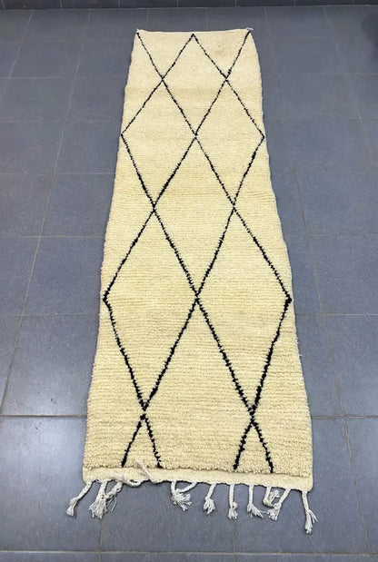 Cream-colored moroccan handmade beni ouarain rug with black geometric diamond patterns and white fringe 2.8m x 0.7m