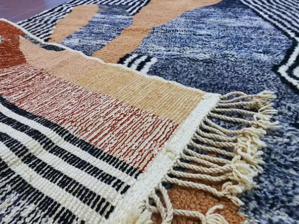 A beni ouarain moroccan handmade rug with bold navy, beige, rust, and black geometric wool patterns and thick fringe
