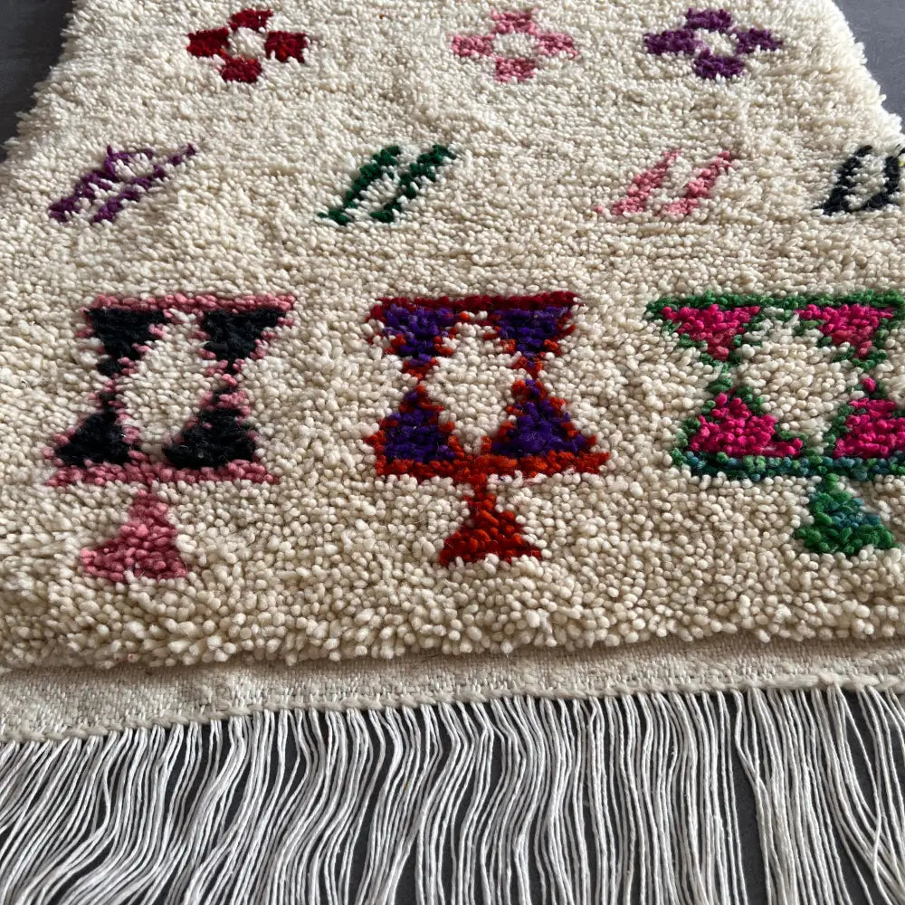 Cream-colored moroccan handmade beni ouarain rug with colorful floral and geometric embroidery and white fringe, 1.10m by 80cm