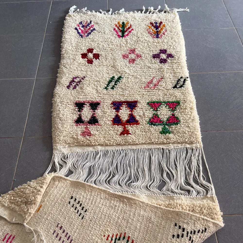 A cream-colored moroccan handmade beni ouarain rug with colorful geometric patterns and white fringe edges by DecorBites
