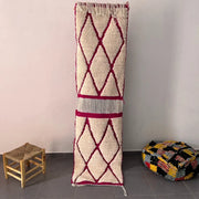 A cream-colored moroccan handmade beni ouarain rug with bold magenta diamonds and textured woven fringe border