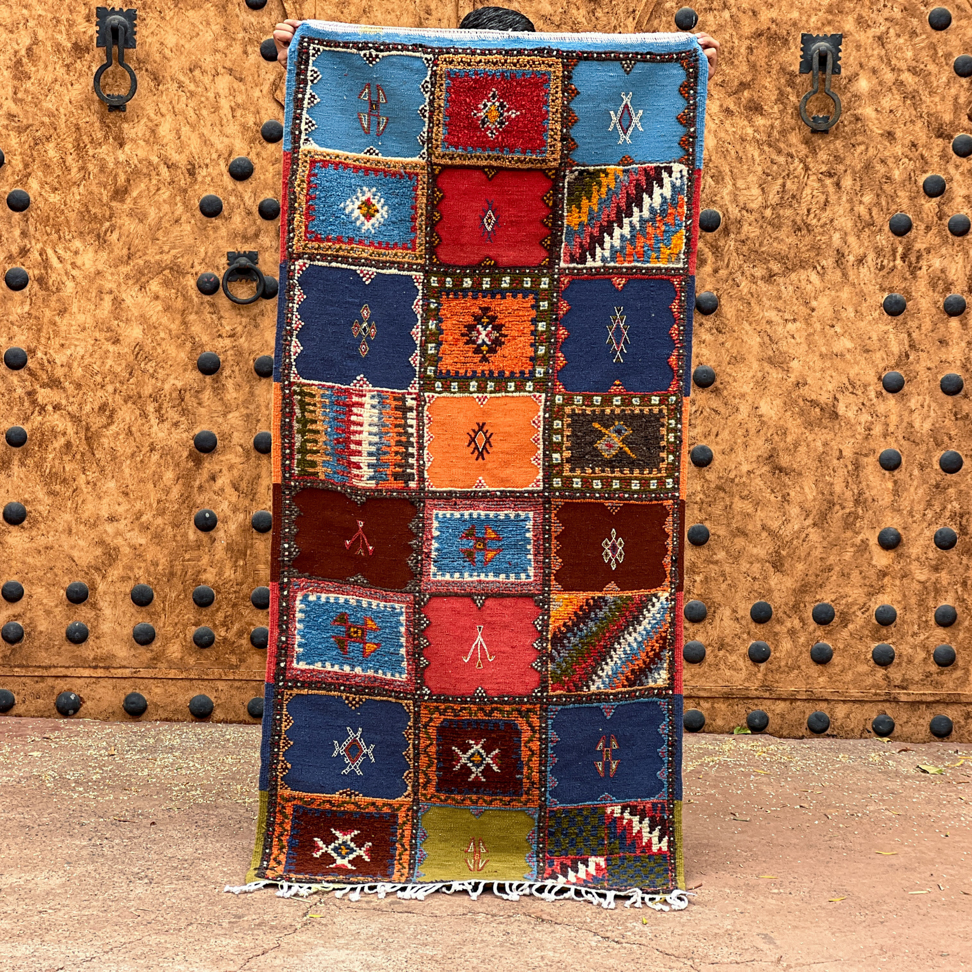 A vibrant moroccan handmade taznakht rug with geometric patterns in blues reds oranges and browns with fringed edges