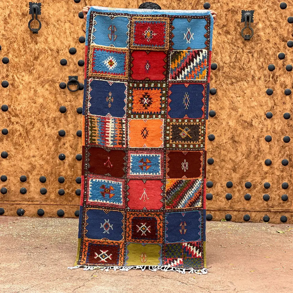 A vibrant moroccan handmade taznakht rug with geometric patterns in blues reds oranges and browns with fringed edges