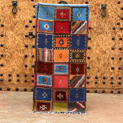 A vibrant moroccan handmade taznakht rug with geometric patterns in blues reds oranges and browns with fringed edges