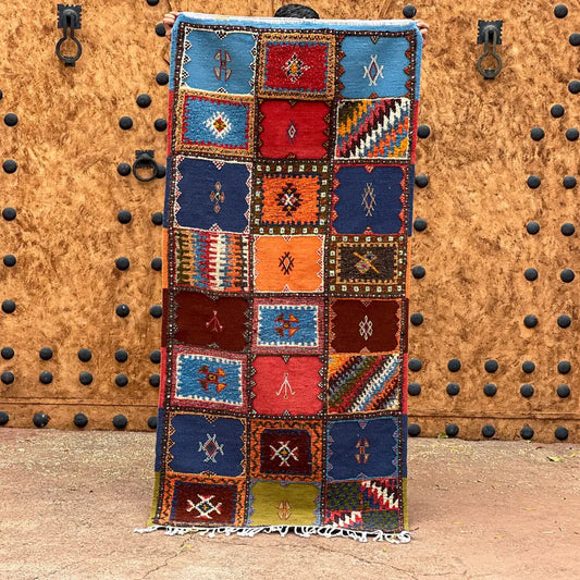 A vibrant moroccan handmade taznakht rug with geometric patterns in blues reds oranges and browns with fringed edges