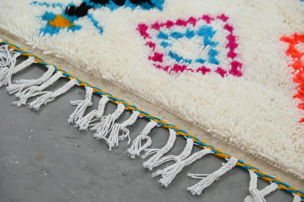 A vibrant cream-colored moroccan handmade traditional azilal carpet with bold geometric patterns and decorative fringe