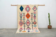 Beige moroccan handmade traditional azilal carpet with vibrant blue red orange and teal geometric patterns on woolen surface