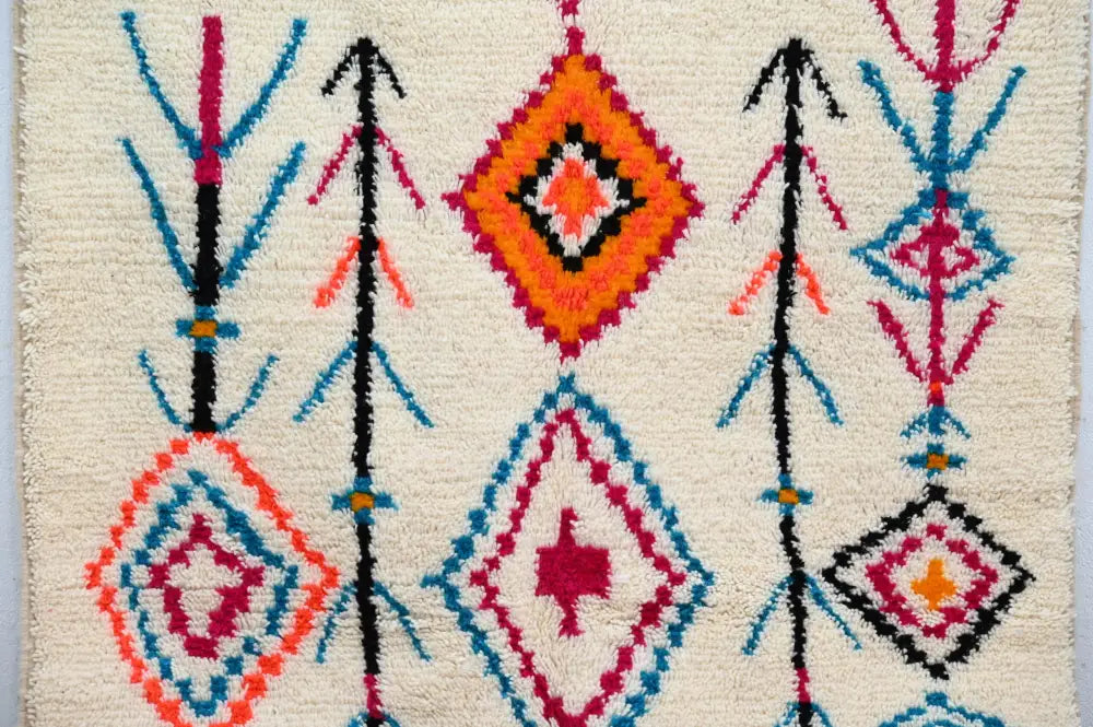 A cream-colored moroccan handmade traditional azilal carpet featuring bold orange pink blue and black geometric patterns