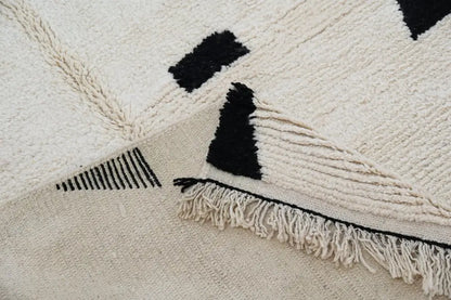 Cream-colored moroccan handmade traditional azilal rug with black geometric patterns and fringed edges by DecorBites