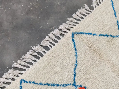 Cream-colored moroccan handmade azilal rug with blue geometric patterns and white fringe made of pure natural wool