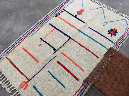 Cream-colored moroccan handmade azilal rug with bold geometric patterns in red blue black orange made of pure natural wool